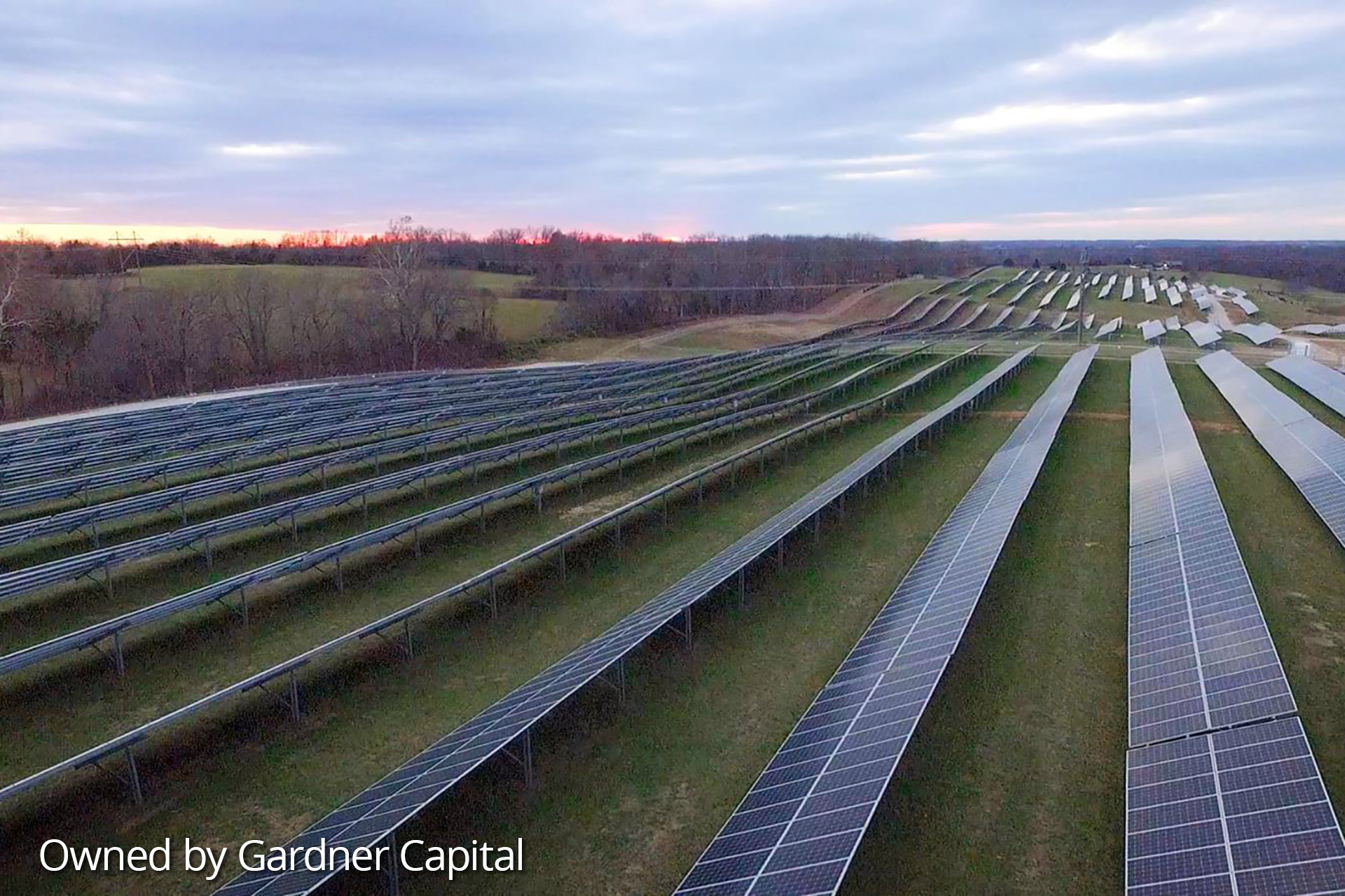 Field of solar panels with trees in the background as the sun is setting at the Nixa Solar project site in Missouri.